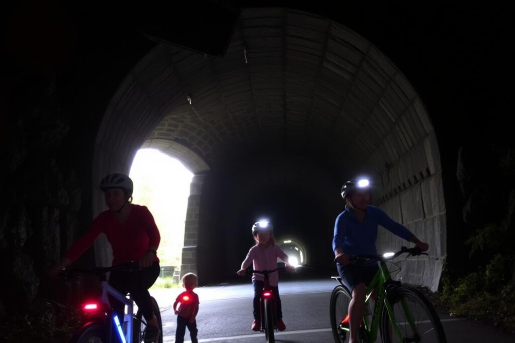 Family with lights on their e-bikes entering the St. Paul Pass Tunnel on Hiawatha Trail Family with lights on their e-bikes entering the St. Paul Pass Tunnel on Hiawatha Trail